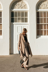 a lady in a black crop top, a trench coat and a pair of beige pants